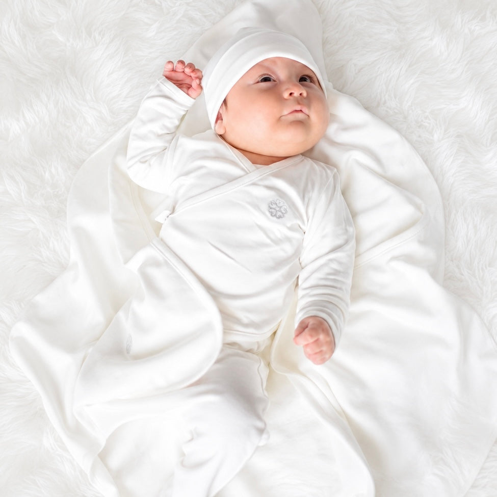 Bebé recién nacido con ajuar Ecowhite puesto — chaqueta cruzada, gorrito y manta 100% algodón Pima orgánico | Rikury