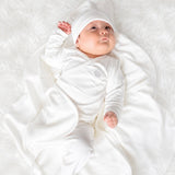 Bebé recién nacido con ajuar Ecowhite puesto — chaqueta cruzada, gorrito y manta 100% algodón Pima orgánico | Rikury