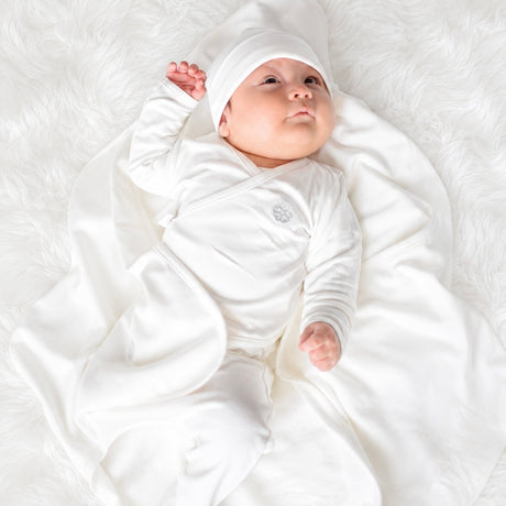 Bebé recién nacido con ajuar Ecowhite puesto — chaqueta cruzada, gorrito y manta 100% algodón Pima orgánico | Rikury